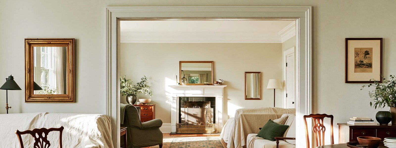 New pale gray drywall hung square and flush across one end of a lived-in room, the joints still open and unfinished, a stepladder folded against the far wall and a canvas drop cloth over the floor